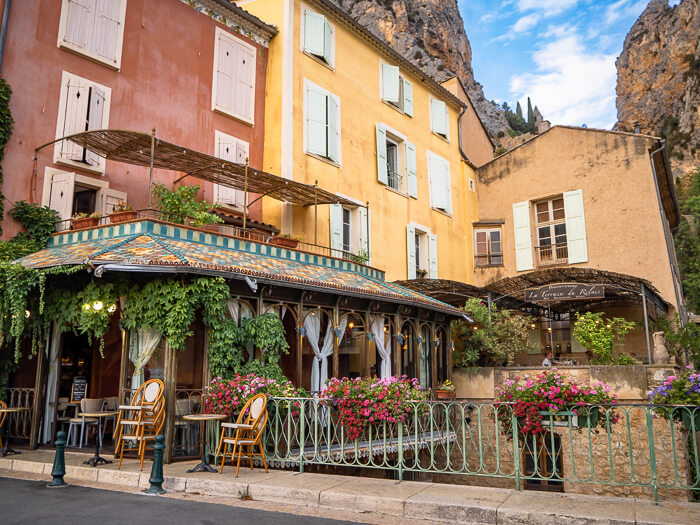 Colorful houses and flower-adorned balconies at Moustiers-Sainte-Marie village with mountains in the background.