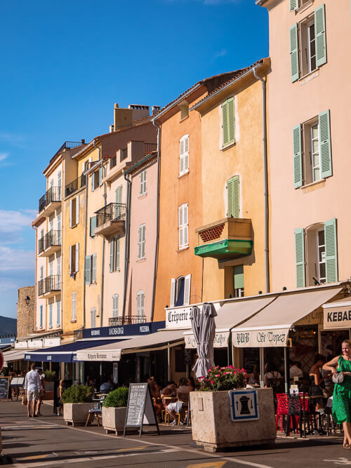 Pastel-colored houses and small cafes at Saint-Tropez waterfront with blue sky in the background.