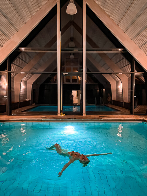 a woman floating on her back in a turquoise pool at the spa of Thorseng Nature Resort in Denmark