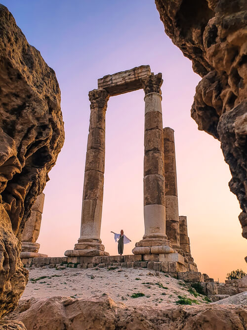 A woman standing between ancient tall columns at Amman Citadel during sunset