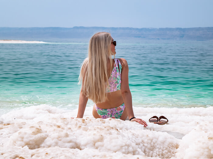 A woman sitting on a Dead Sea beach covered with white salt formations