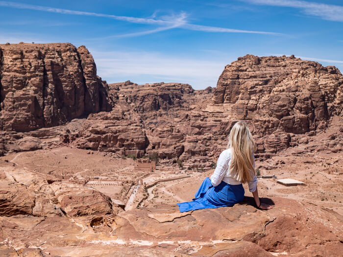 A woman sitting on a rock overlooking the archaeological site of Petra