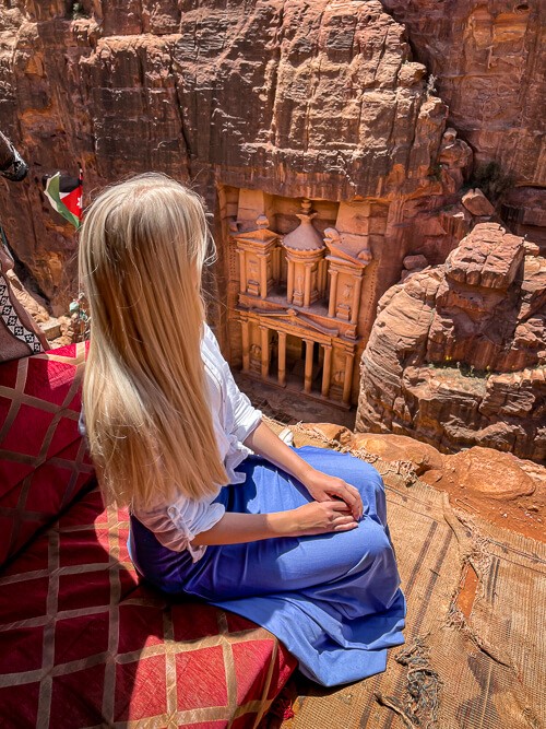 A woman sitting on a cliff overlooking the Treasury in Petra, a mandatory stop in every 10-day Jordan itinerary