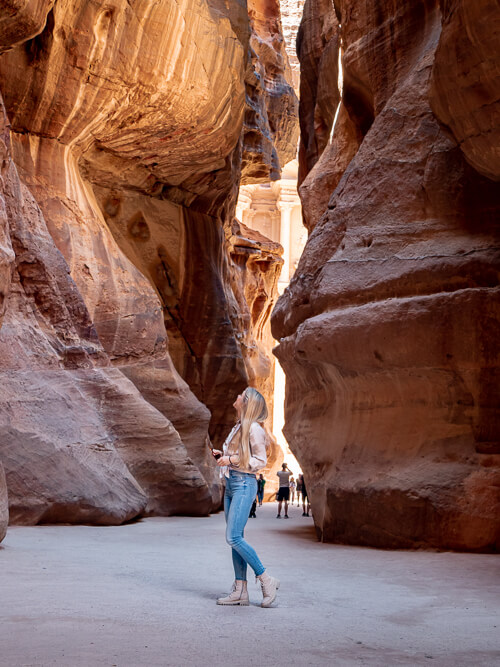 A woman standing in the middle of The Siq, a narrow canyon in the Lost City of Petra, Jordan