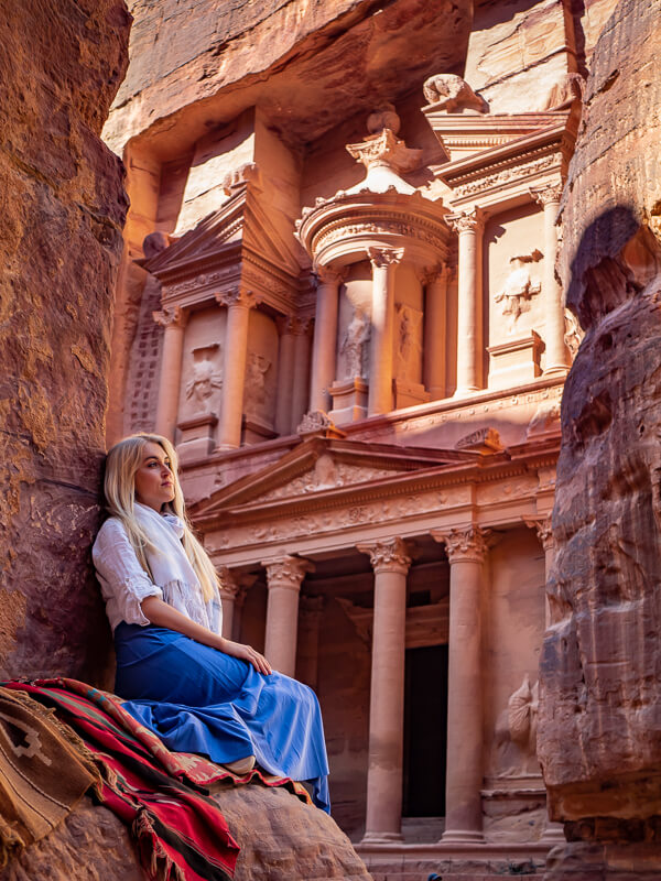 A woman sitting on a rock in front of the Treasury monument in Petra, a must-visit attraction on every Jordan itinerary