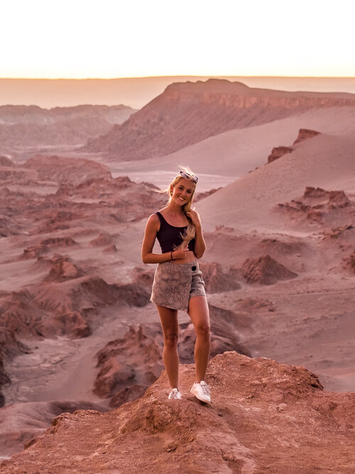 A woman standing on the edge of a cliff with a backdrop of the rugged landscapes of the Atacama Desert