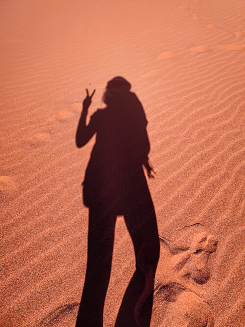 A shadow of a woman on orange rippled sand in Jordan