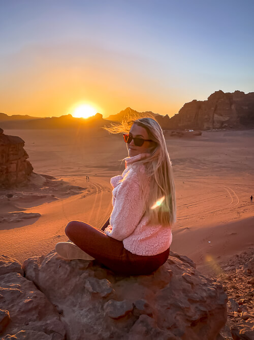 Me sitting on a rock and admiring the sunset in Wadi Rum with red desert landscapes in the background.
