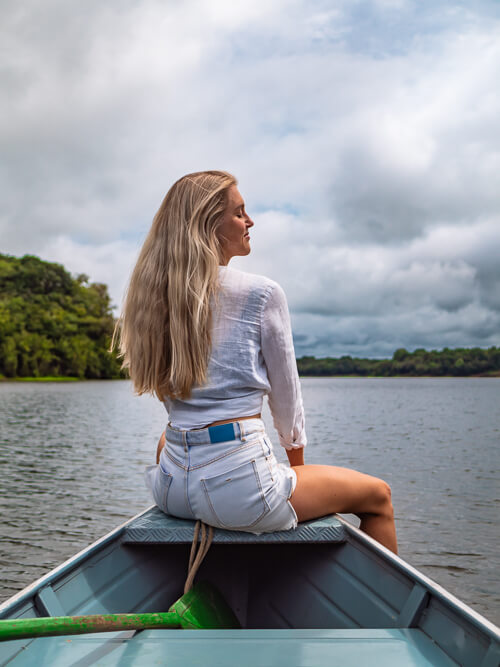 a woman sitting at the front of a boat cruising on a river in the Amazon jungle in Brazil