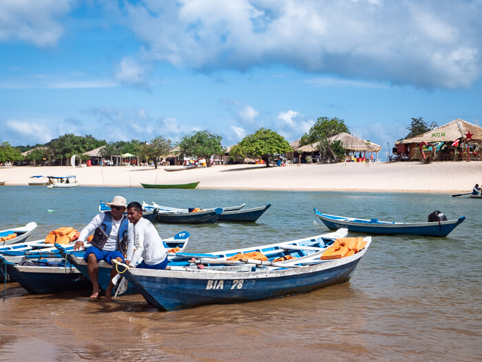two men sitting on wooden boats in front of the sandy Ilha do Amor beach in Alter do Chao, Brazil