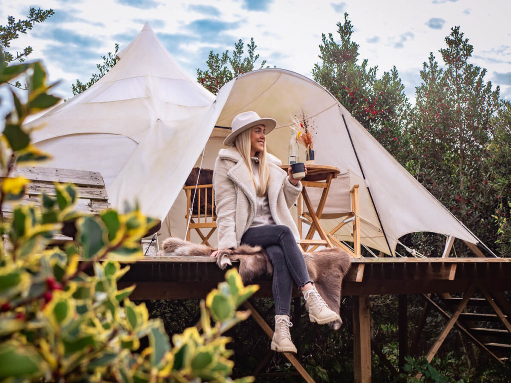 A woman sitting on a terrace in front of a white tent at one of the best spots for glamping in Denmark