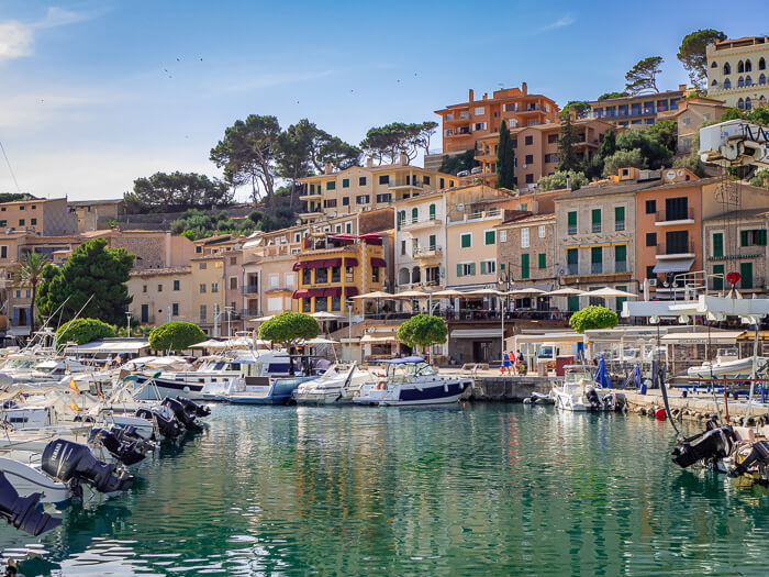 Boats docked in Port de Soller marina with a backdrop of pastel-colored traditional buildings.