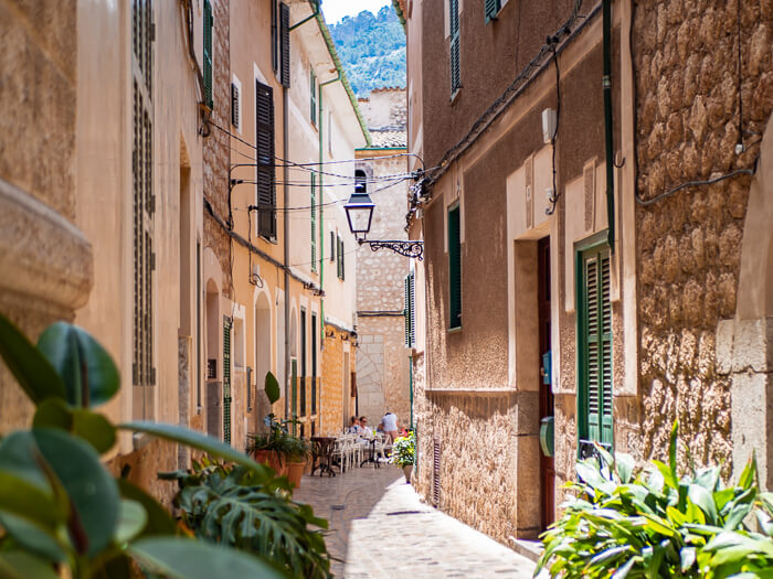 A narrow cobblestone alley between traditional Mallorcan houses with stone walls and green shutters in Soller.