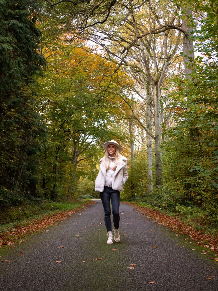 a woman walking in the middle of a road in a lush green forest in South Funen