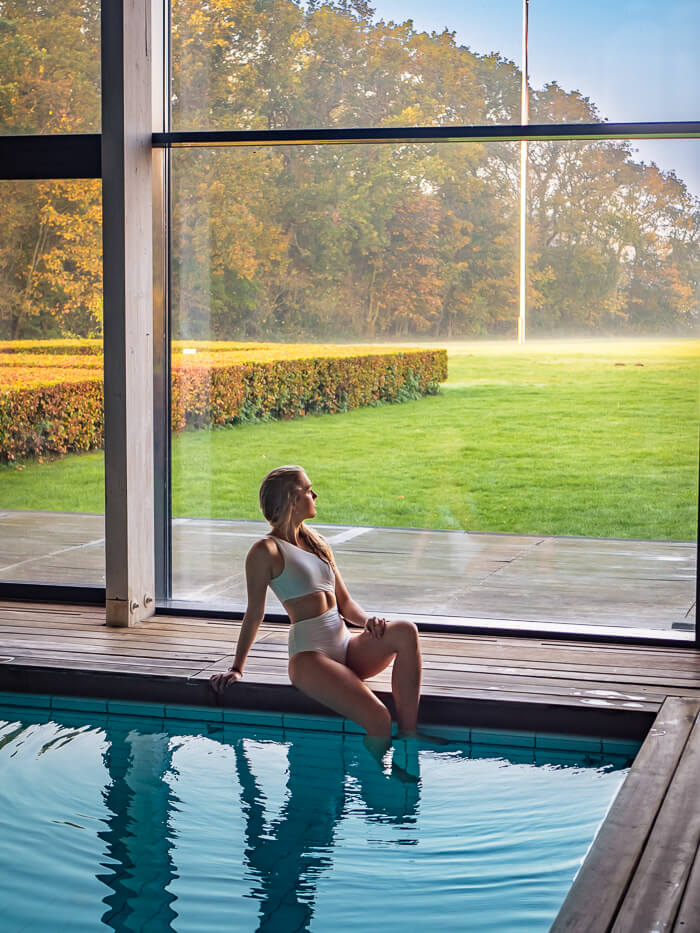 A woman sitting on the edge of an indoor pool and gazing out of a window at Thorseng Nature Resort