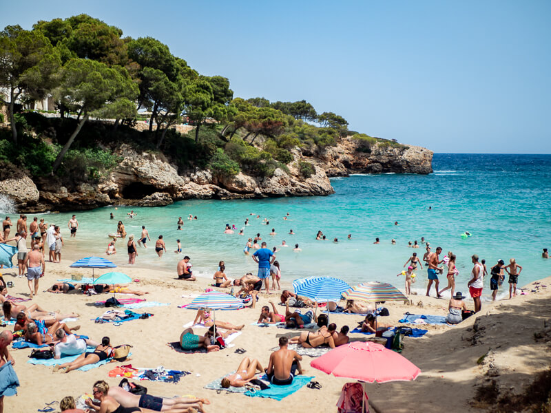A sandy beach full of holidaymakers, colorful parasols and beach towels in Mallorca, Spain