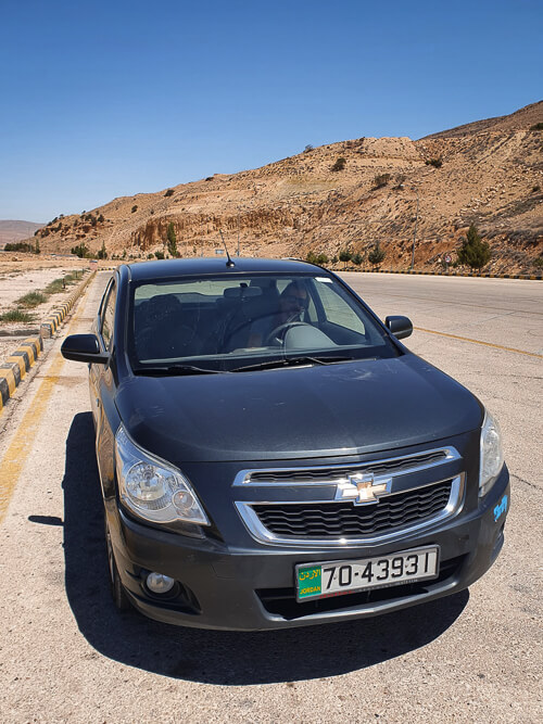 A black rental car parked in a desert in Jordan