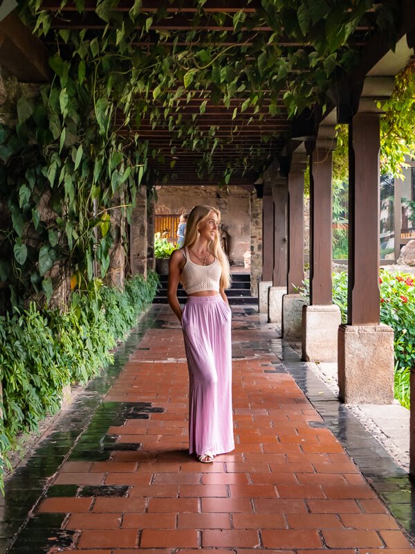 A woman standing in a hallway surrounded by lush vegetation at Hotel Casa Santo Domingo in Antigua Guatemala.