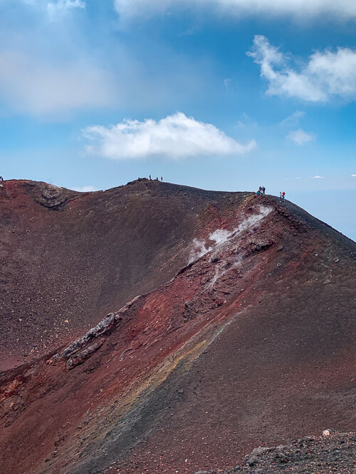 Red volcanic sand and steaming ground at a crater on Mount Etna tour