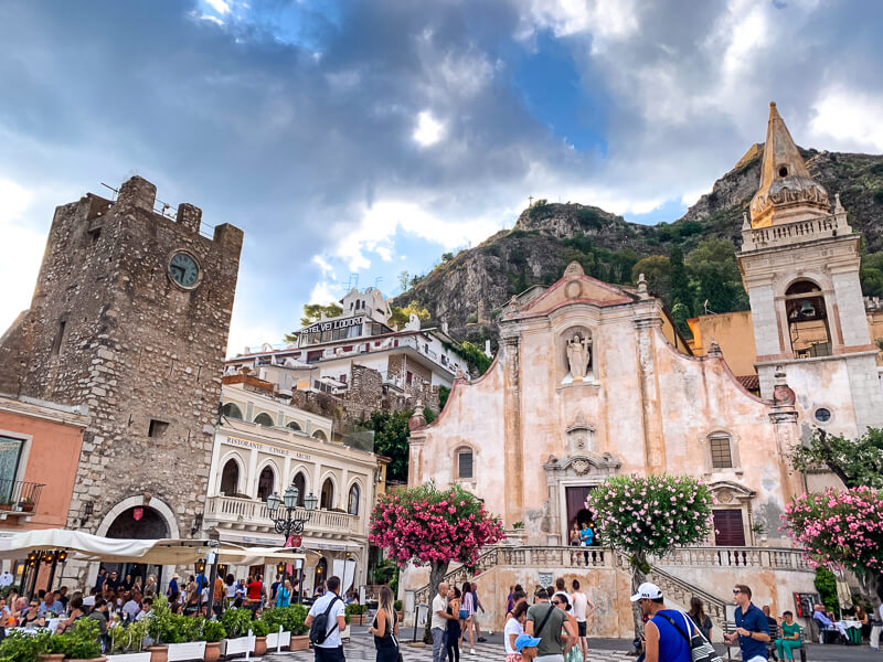 Medieval buildings, blooming flowers and crowds of tourists on the central square of Taormina, one of the most beautiful towns in this Sicily 7 day itinerary.