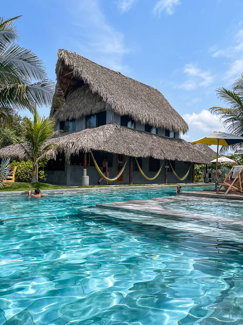 a large swimming pool and a thatched-roof house in Cocori Lodge beachfront hotel