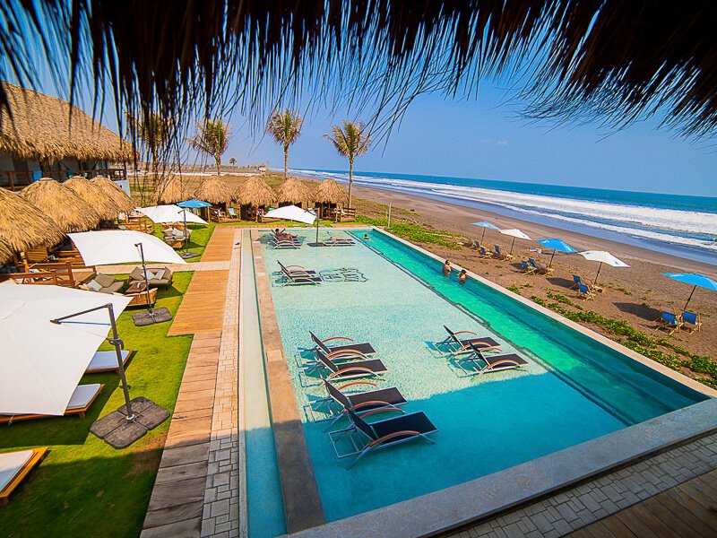 A swimming pool with sun loungers in it, overlooking the Pacific Ocean at Playa 14 beach club