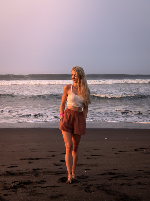 A woman standing on a black sand beach with ocean waves in the background