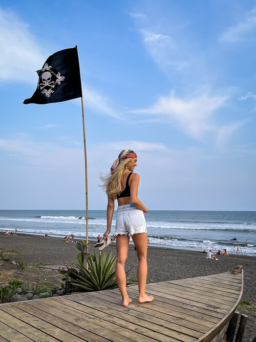 A woman standing on a wooden deck overlooking a black sand beach in Guatemala