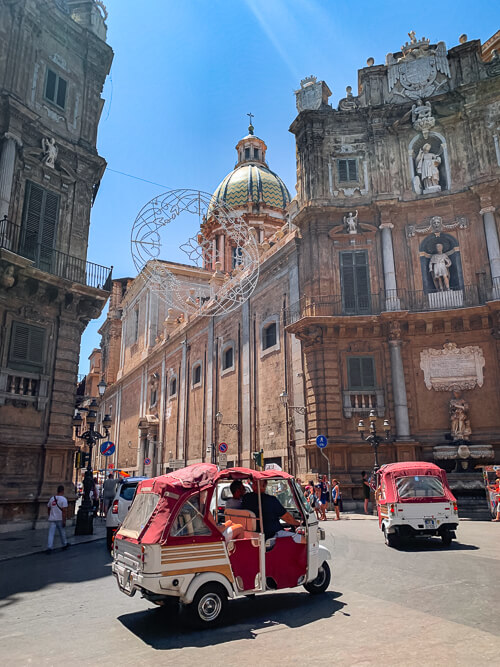 Red tuk-tuks driving through Quattro Canti swuare in the center of Palermo old town