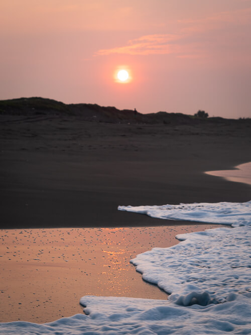 Pink sky and a black sand beach during sunrise