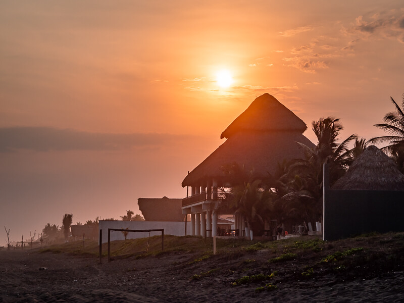 sun setting behind a house with a thatched roof on Playa El Paredon beach in Guatemala