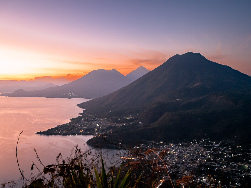 a panoramic view of volcanoes and small towns around Lake Atitlan during sunrise, one of the best places to visit in Guatemala