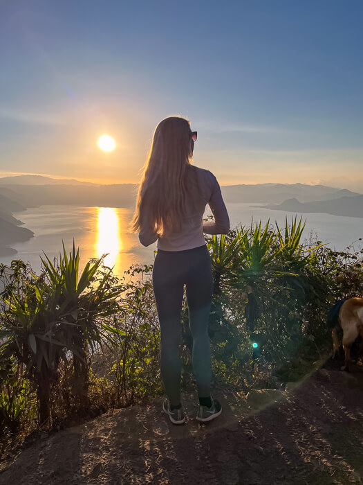 A woman standing on the Indian Nose peak, gazing at the sunrise over Lake Atitlan