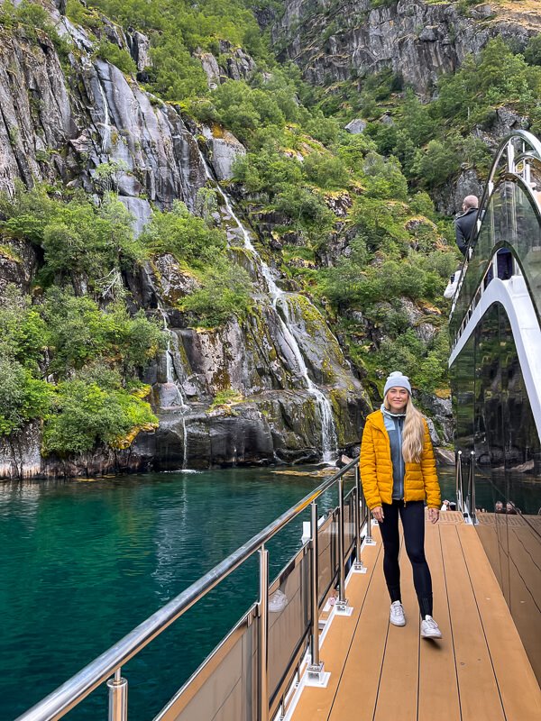 A woman standing on an eco-friendly electric catamaran in front of a waterfall in Trollfjord