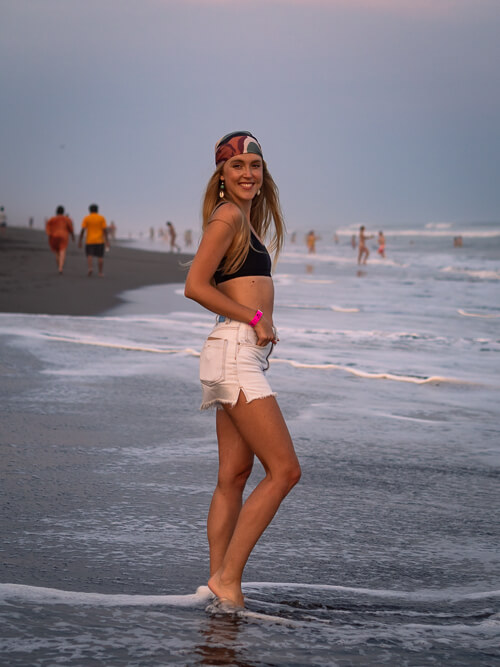 a woman standing in shallow water on the black sand beach of El Paredon in Guatemala