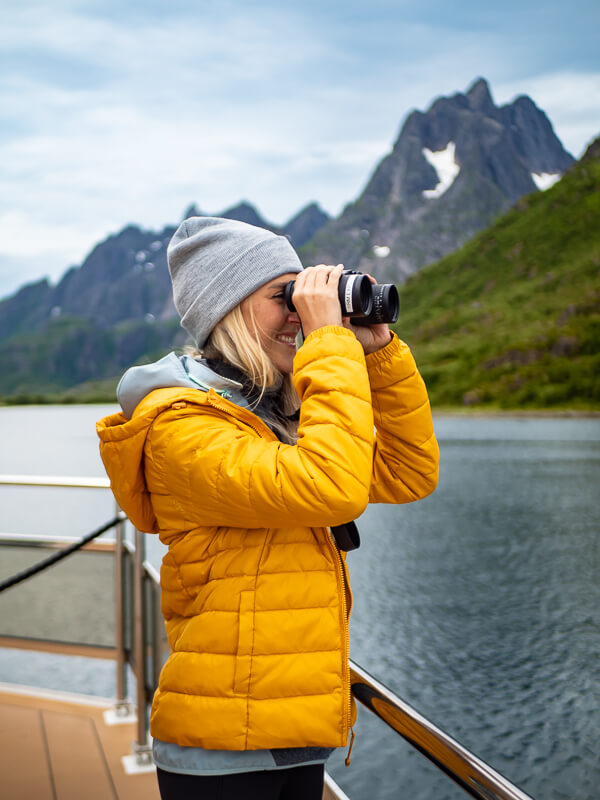Me in a yellow jacket using binoculars to spot sea eagles on a Trollfjord tour in Norway