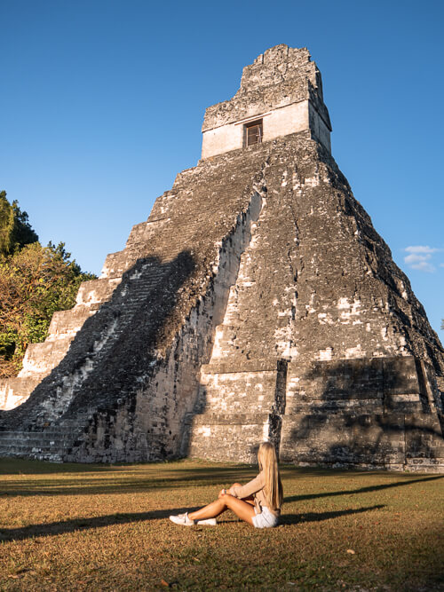 A woman sitting on the ground in front of the Mayan Temple of the Great Jaguar in Tikal National Park