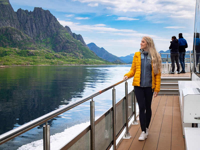 A woman standing on the deck of a modern hybrid-electric ship by Brim Explorer on a Silent Trollfjord Cruise