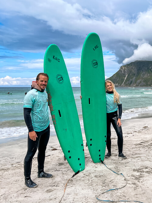 Me and my boyfriend standing on a sandy beach with our surf boards at Lofoten Beach Camp