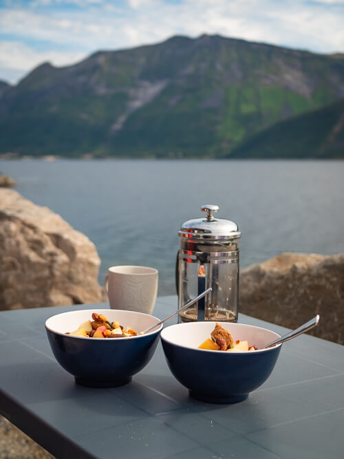 Two breakfast bowls and a coffee mug with a backdrop of a beautiful Norwegian fjord