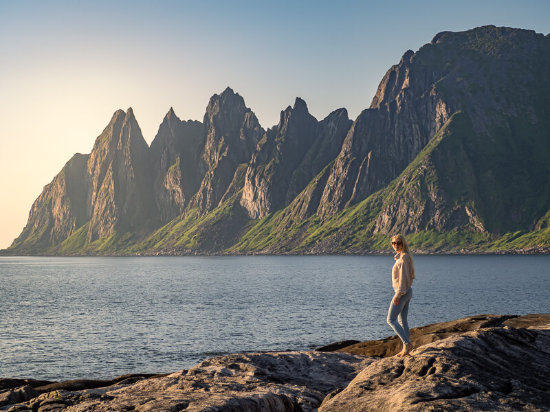 A woman standing on a rock with a backdrop of steep jagged mountains on  Senja island, Norway