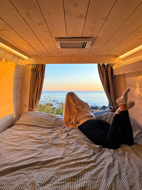 A woman lying on the bed of a campervan rented from Wecamp in Norway