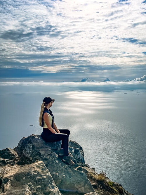 A woman sitting on a rock with a panoramic view of the sea around Lofoten Islands