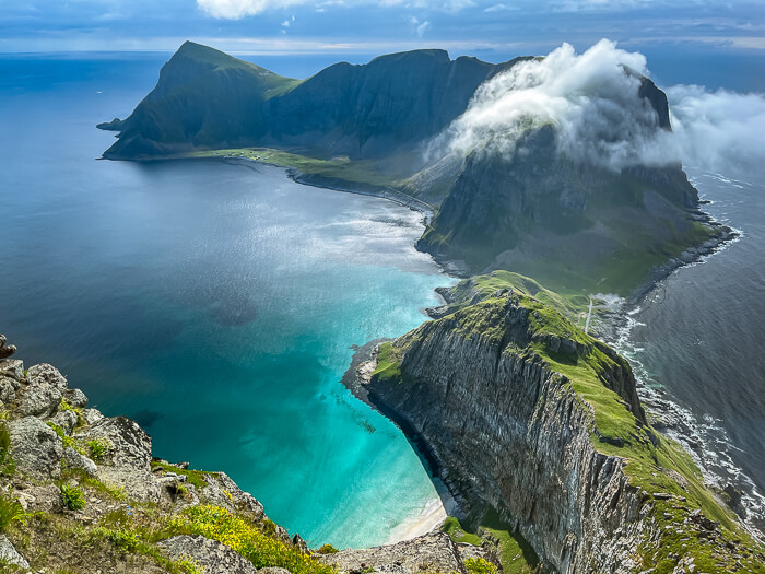 A steep mountain ridge rising out of turquoise sea at Værøy island, viewed from Håen peak, one of the best hikes in Lofoten, Norway.
