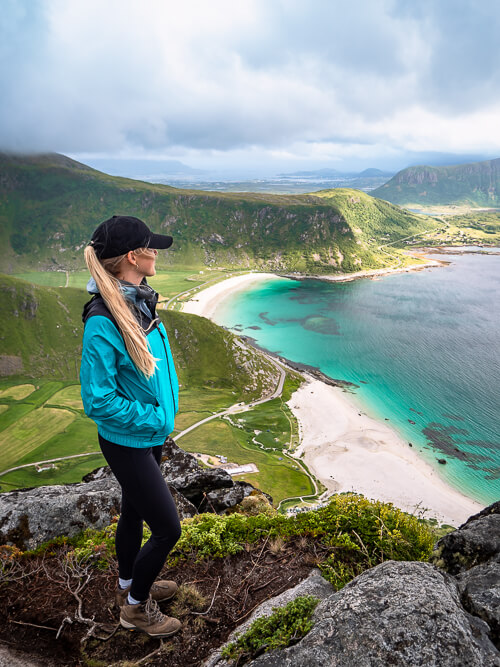A woman standing on top of the Mannen peak with a view over Haukland Beach with its blue-green water and white sand