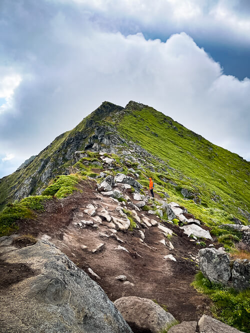 A rocky hiking trail leading to the top of Mannen with dark rain clouds above it