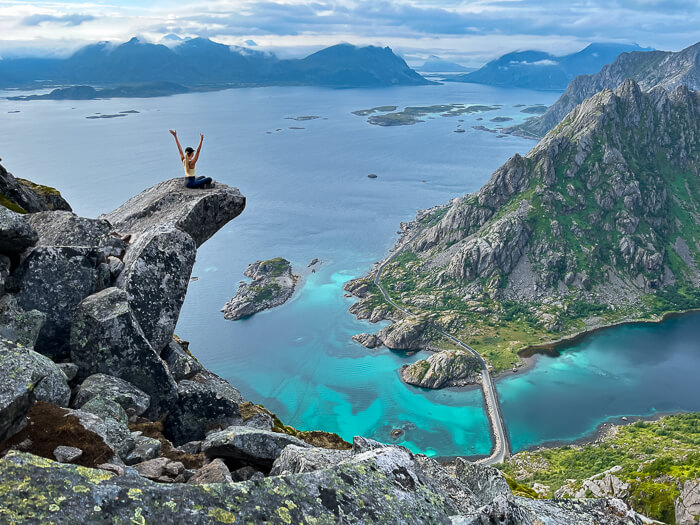 A woman sitting on a rock protruding from mountainside at Torsketunga, one of the most unique hikes in Lofoten