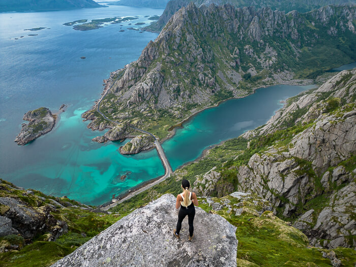 A woman standing on a rock overlooking a picturesque fjord with turquoise water at the Torsketunga hike
