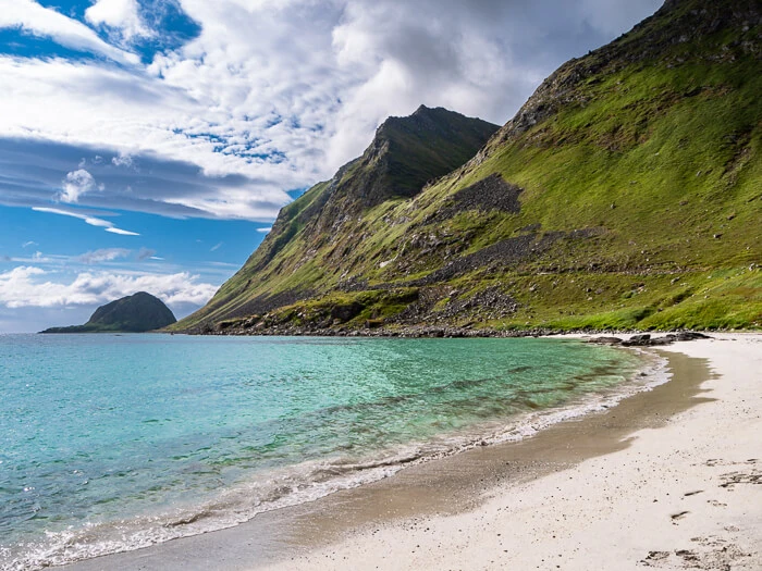 Blue-green water, soft sand and a green mountain as a backdrop at Haukland Beach on a sunny summer day