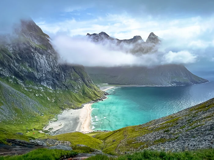 Steep green mountains surrounding the white sand and turquoise water of Kvalvika Beach, one of the highlights of this 5-day Lofoten Islands itinerary